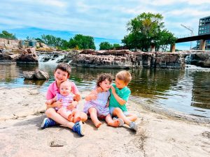 Four kids of a Sioux Falls real estate agent. two boys and two girls sitting on a rock in front of the Falls at the Falls Park in Sioux Falls, South Dakota.